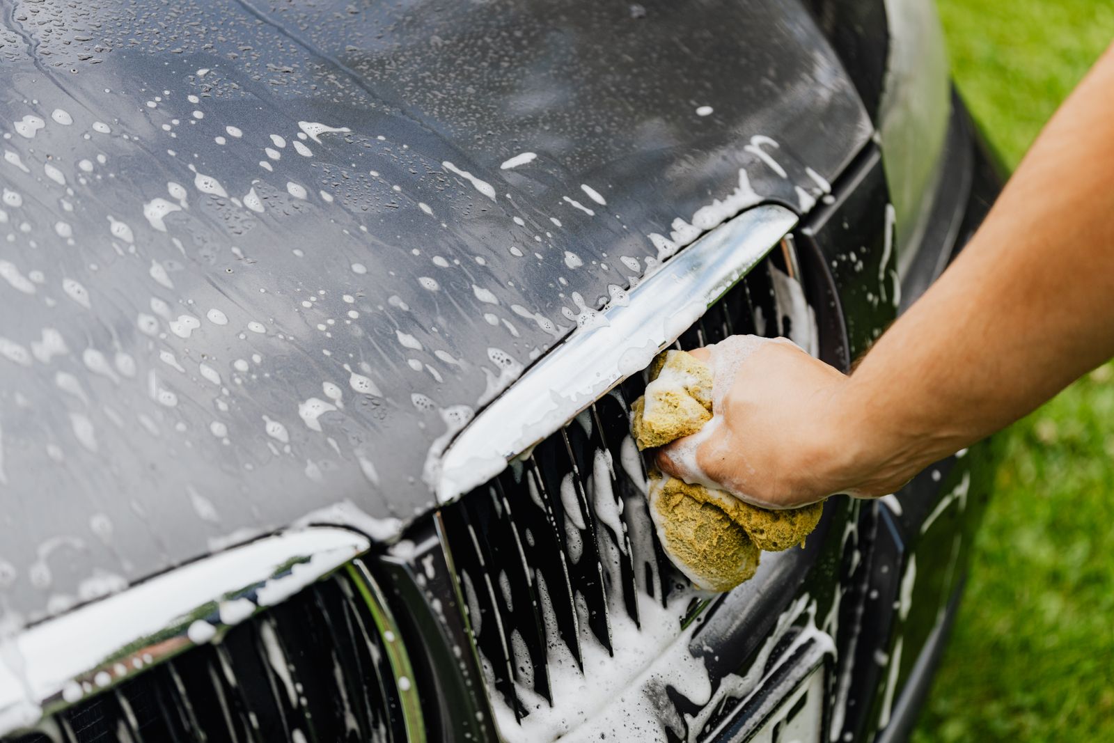 Hand washing a car grille with a soapy sponge
